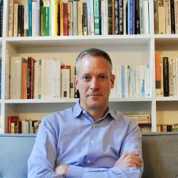 White man in blue shirt in front of books