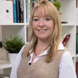 White woman with blonde hair wearing a brown vest