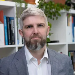 White man with brown beard in a grey suit jacket