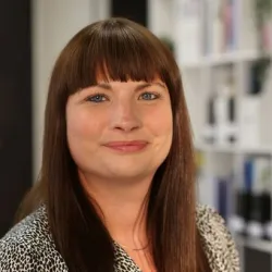 White woman with brown hair and a fringe wearing a white shirt