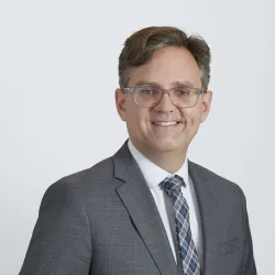 Smiling white man with black and grey hair in a grey suit