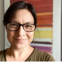 Photograph of a white woman with tied back brown hair and glasses on, smiling