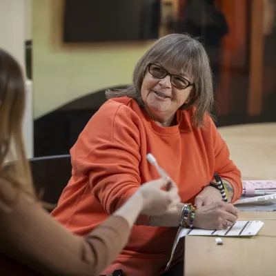 Woman with orange jumper speaking to another woman