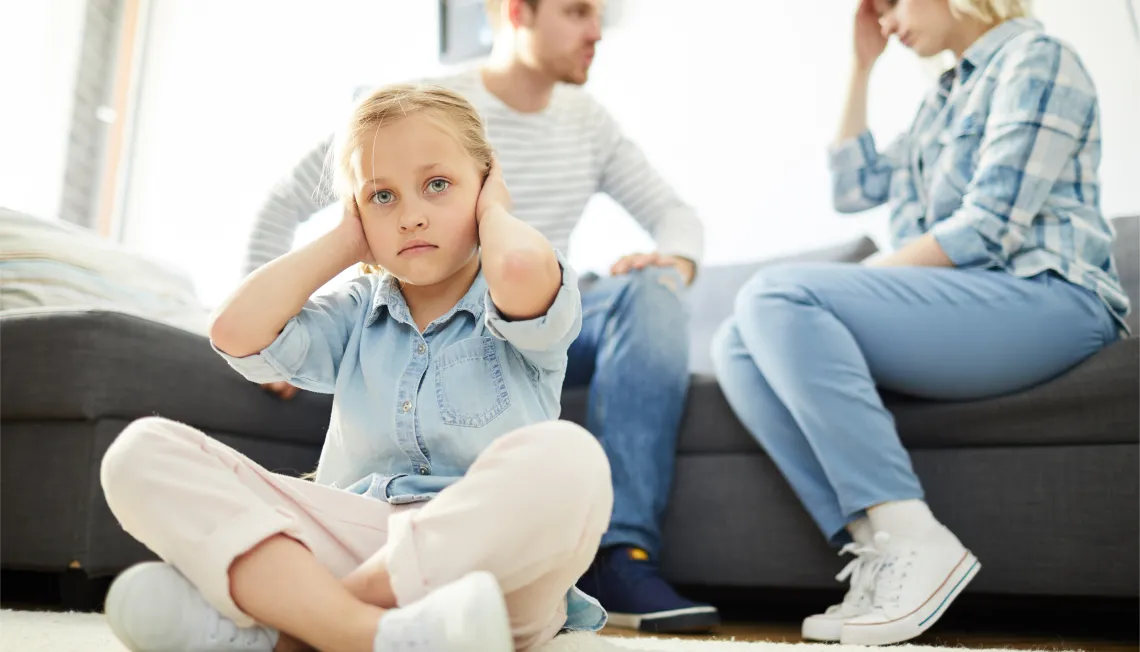 Child covering ears with parents arguing in the background